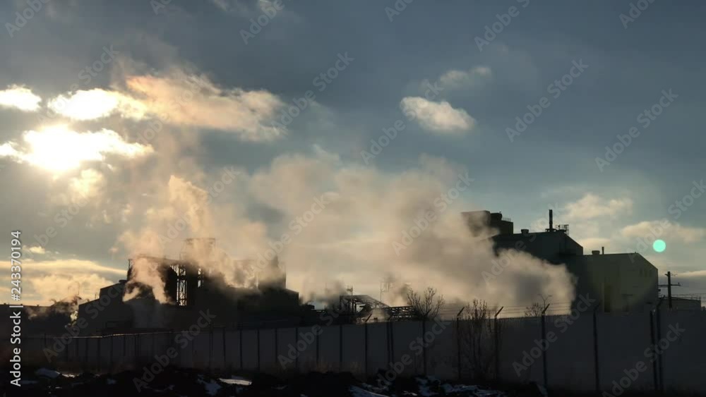 Industrial pollution in winter as hot steam and smoke are emitted into air moving sideways with late afternoon sun hovering above. Industrial pollution in winter as hot steam and smoke are emitted into air moving sideways with late afternoon sun hovering above.