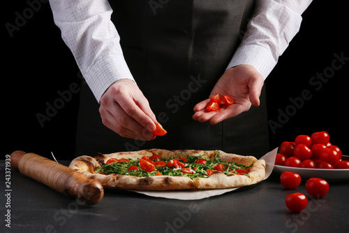 chef put ingredients on pizza. chef in apron and white shirt decorating pizza with tomatoes cherry and arugula