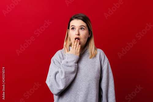 Portrait of shoked young girl in pink sweater looking away with mouth covered