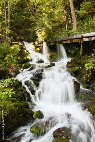 Wasserfall eines Baches mit Holzsteg und Langzeitbelichtung im Wald