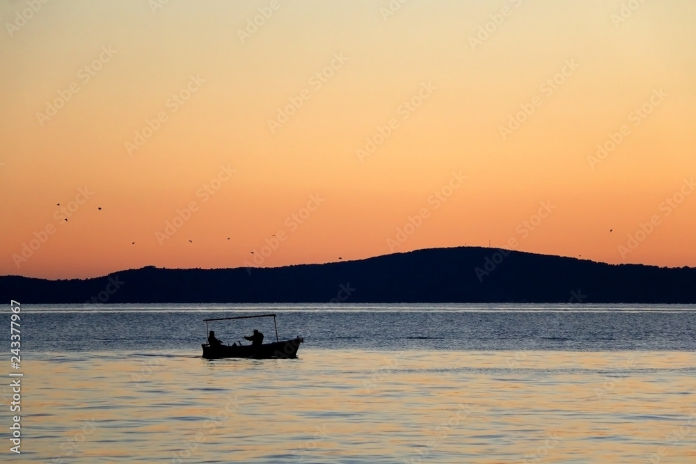 Silhouete of a small fishing boat and birds during suset. Beautiful sunset above the sea. 