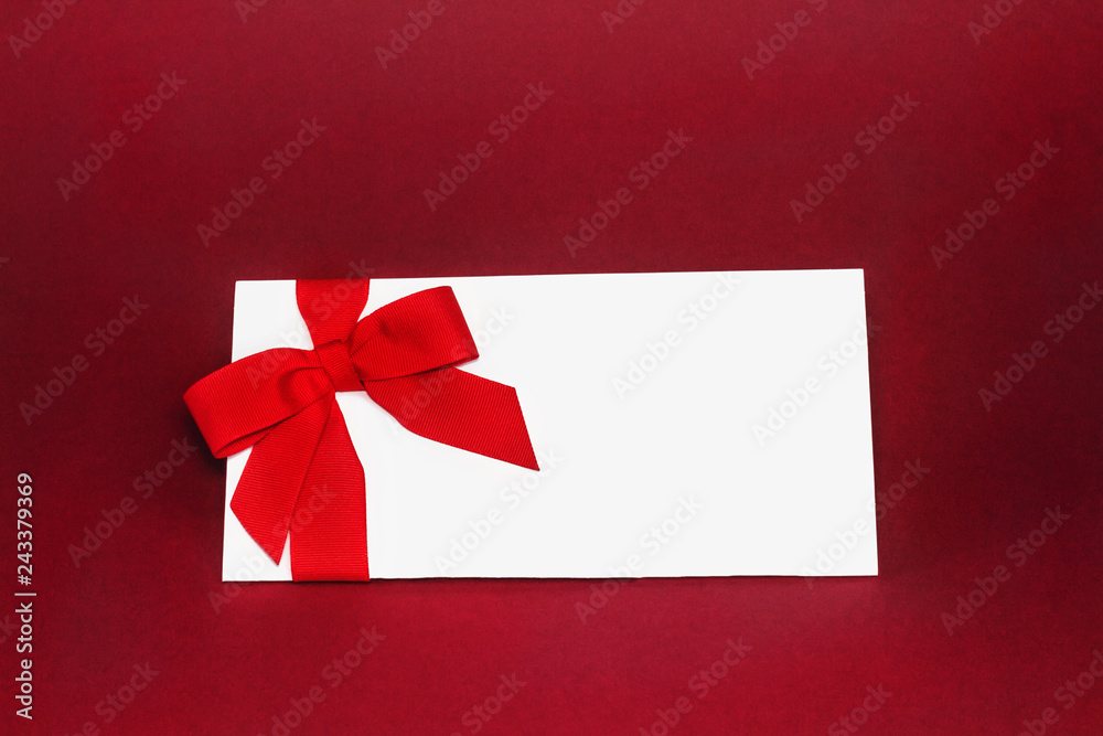 Isolated white gift card with red ribbon bow on deep red background. Isolated white gift card with red ribbon bow on deep red background.