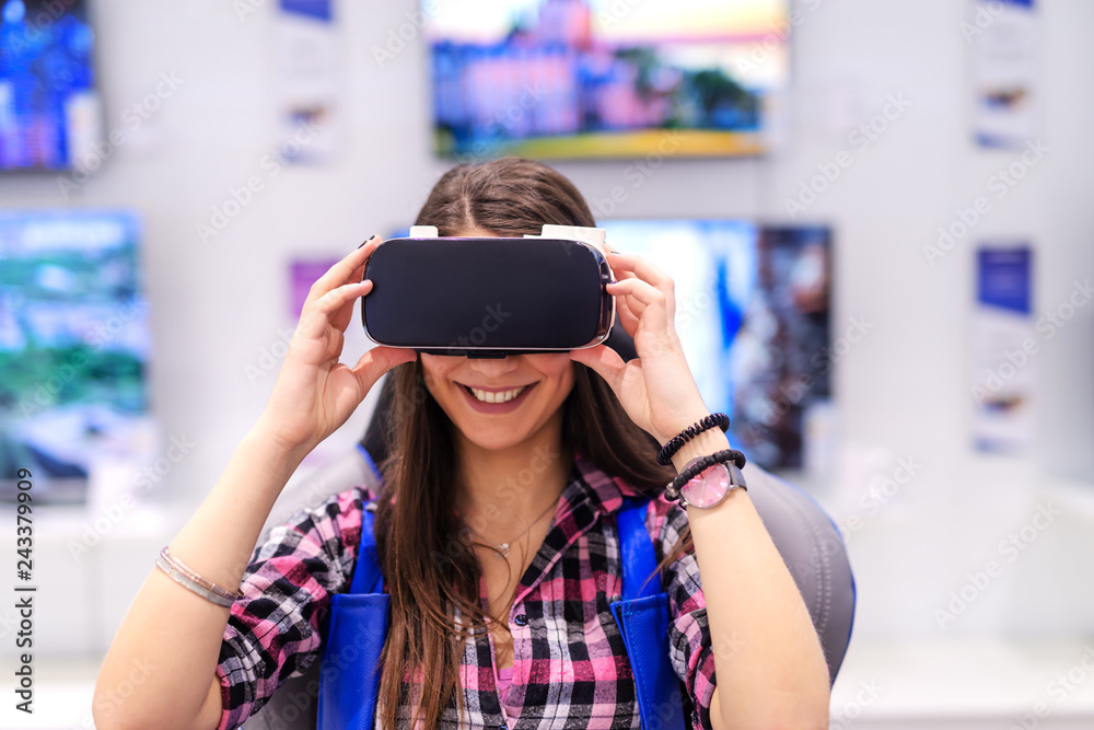 Excited smiling Caucasian brunette with long hair having trying out virtual reality technology while sitting on the chair in tech store.