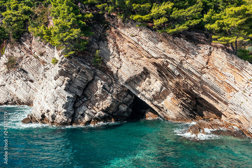 Coast with layered stone, turquoise water, water an trees, suny day