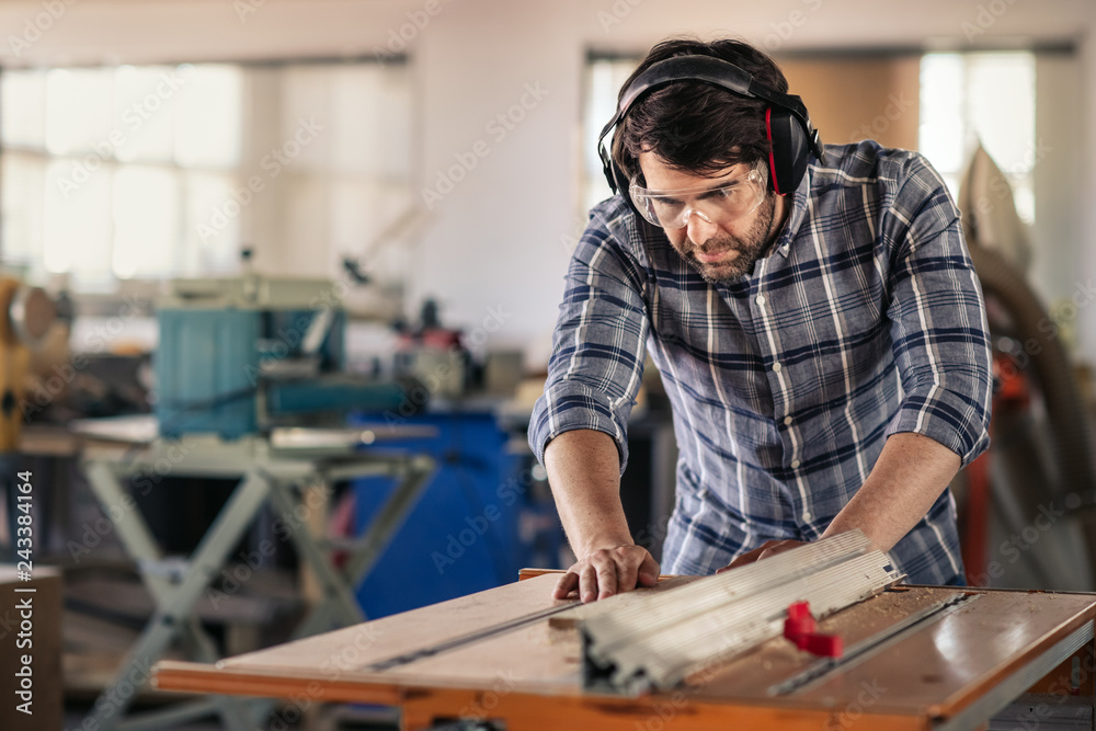 Carpenter sawing wood with a table saw in his workshop Carpenter sawing wood with a table saw in his workshop