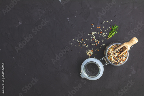 Black, purple, and white rice (Oryza sativa) mix in glass jar on black stone concrete textured surface