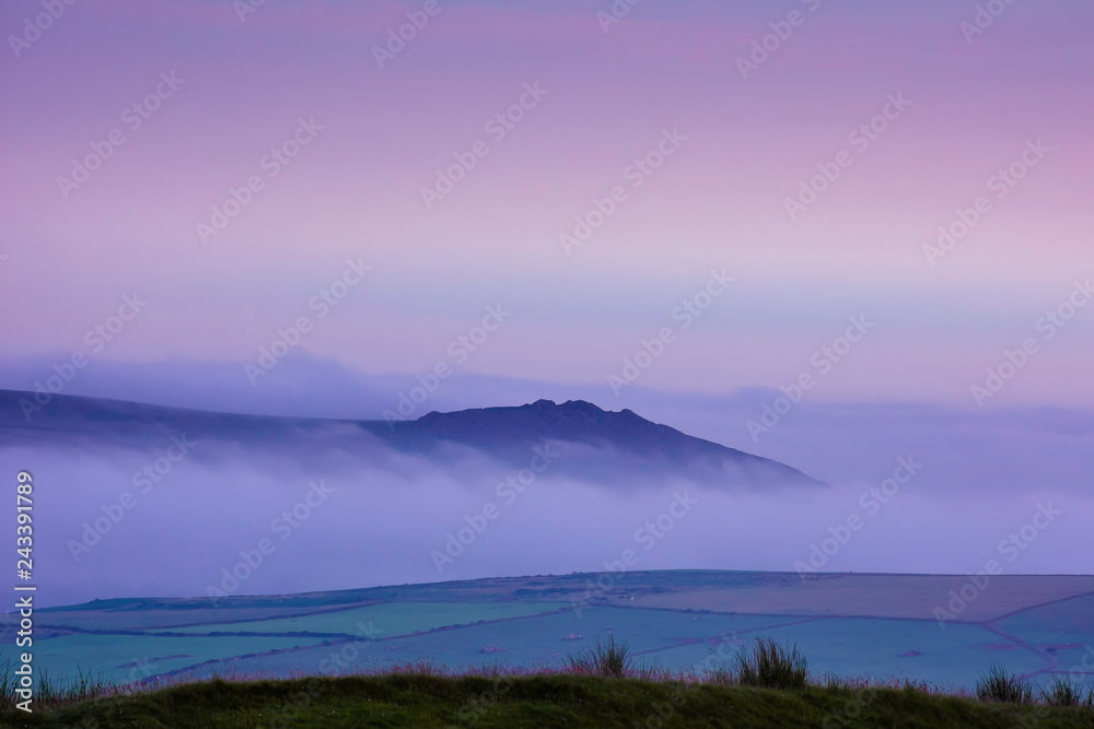 Blue hour on Pembrokeshire moorlands.Hill surrounded by fog in valley and pink sky before sunrise.