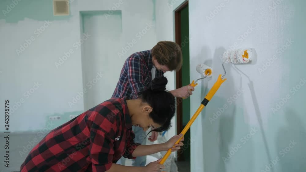 Excited laughing multiracial homeowners renovating their interior design, doing home improvement and renewal together in new empty apartment while painting wall with paint rollers. Excited laughing multiracial homeowners renovating their interior design, doing home improvement and renewal together in new empty apartment while painting wall with paint rollers.