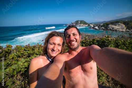 happy couple taking selfie photo in front of the sea in Tayrona National Park, Tropical Colombia. Crazy tourists travelling on the white beach of caribbean sea.  © photomaticstudio