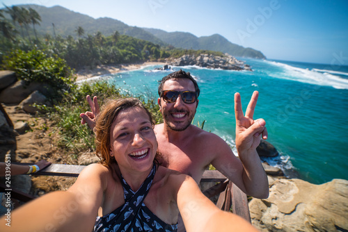 happy couple taking selfie photo in front of the sea in Tayrona National Park, Tropical Colombia. Crazy tourists travelling on the white beach of caribbean sea.  © photomaticstudio