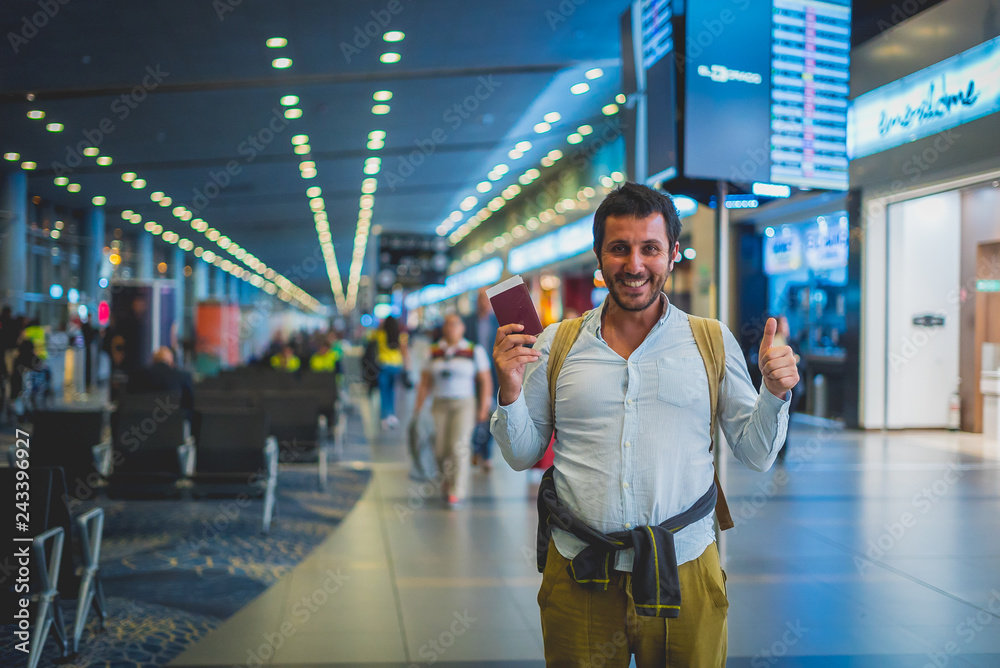 smiling man waiting in the airport, holding tickets and passport and saying OK