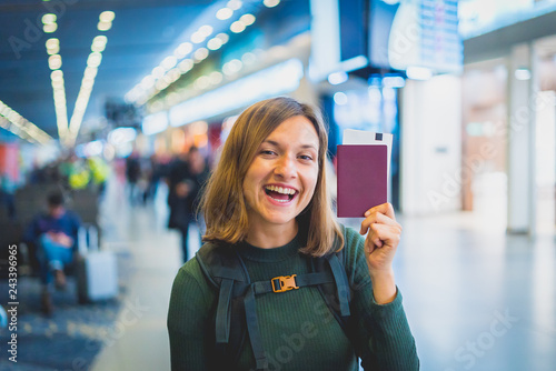 Beautiful young tourist girl in international airport, taking selfie with passport and boarding pass ready for boarding and fly. Doing gesture 