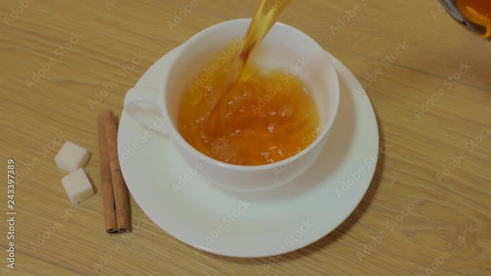 Preparation of black tea, pouring tea in cup from teapot. Drinking hot tea on breakfast in the morning. Wooden table, spices, sugar, cinnamon. Preparation of black tea, pouring tea in cup from teapot. Drinking hot tea on breakfast in the morning. Wooden table, spices, sugar, cinnamon.