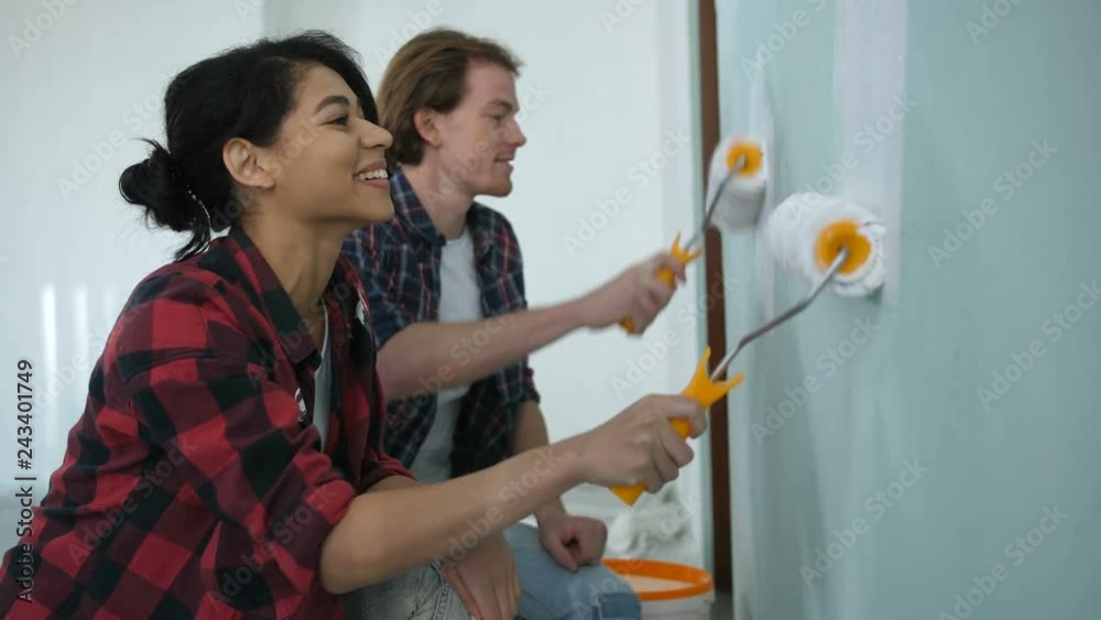 Cheerful diy couple making repair, home makeover and improvement painting interior wall with paint rollers together. Positive family stained in paint, renovating design and painting wall in new house. Cheerful diy couple making repair, home makeover and improvement painting interior wall with paint rollers together. Positive family stained in paint, renovating design and painting wall in new house.