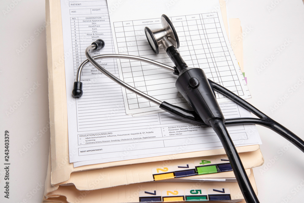 A stack of color-coded and numbered folders containing patient's medical records with blank doctor's visit form, ledger card, and stethoscope set on white background in horizontal image format. A stack of color-coded and numbered folders containing patient's medical records with blank doctor's visit form, ledger card, and stethoscope set on white background in horizontal image format.