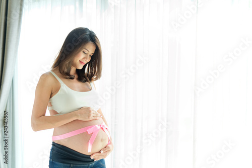 Pink ribbon on young Asian pregnant belly. She putting her hands on stomach between the ribbon and face down looking on her belly which her baby is inside with love. Touching of love from mother. Free Download Pink ribbon on young Asian pregnant belly. She putting her hands on stomach between the ribbon and face down looking on her belly which her baby is inside with love. Touching of love from mother. - GFXLoad