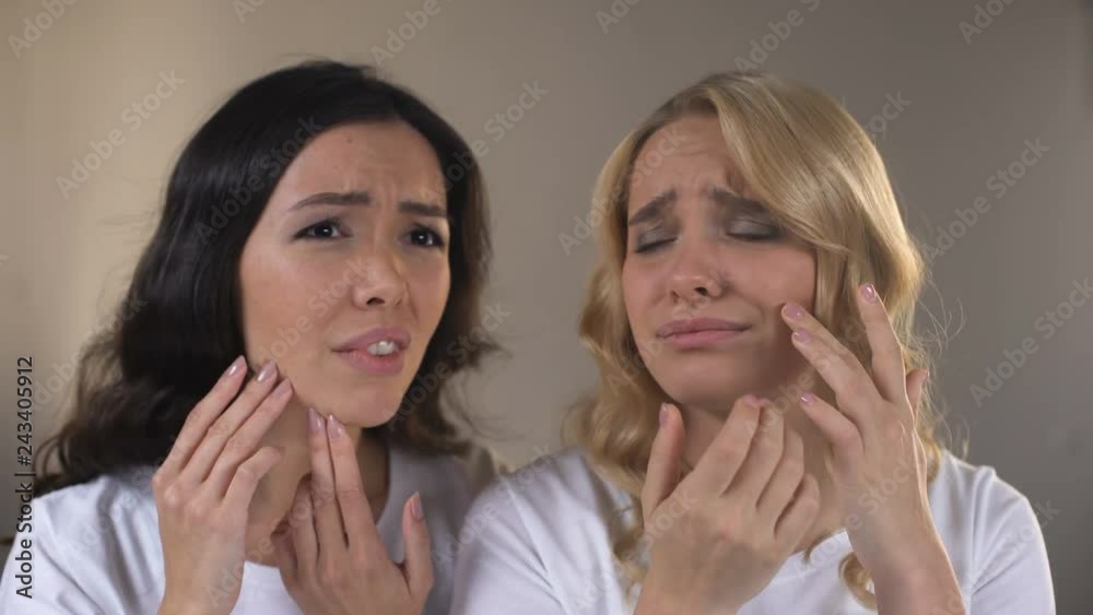 Teen female friends looking in mirror, noticing pimples on face, problem skin Teen female friends looking in mirror, noticing pimples on face, problem skin