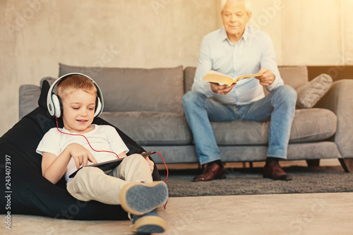 Foto Little boy watching playing on tablet while grandfather reading book