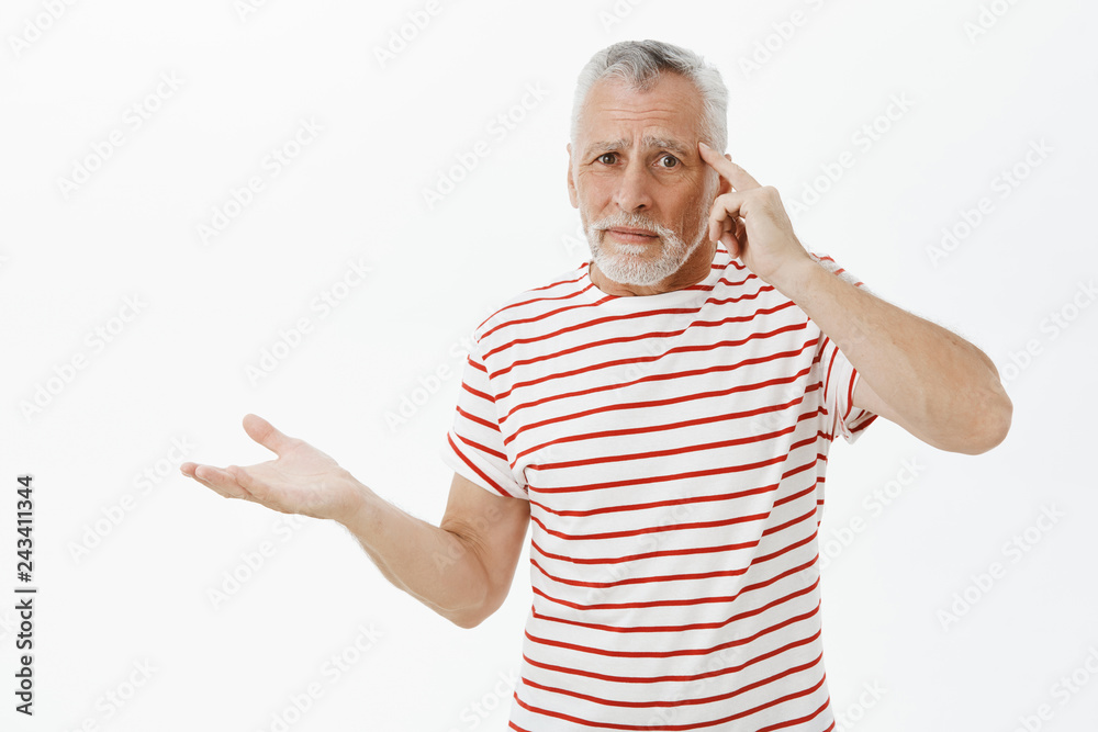 Are you out of your mind. Upset mature dad with white hair and beard in striped t-shirt raising palm in clueless gesture rolling index finger on temple being disappointed in person acting crazy Are you out of your mind. Upset mature dad with white hair and beard in striped t-shirt raising palm in clueless gesture rolling index finger on temple being disappointed in person acting crazy