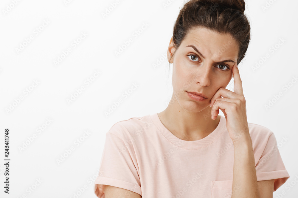Close-up shot of concerned displeased young mother leaning on finger frowning and looking thoughtful at camera as trying understand how solve problem standing troubled over gray background Close-up shot of concerned displeased young mother leaning on finger frowning and looking thoughtful at camera as trying understand how solve problem standing troubled over gray background