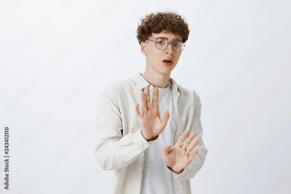 Guy begging bullies not beat him raising hands in surrender trying prevent punch in face standing intense, insecure stepping backwards as wanting run posing unconfident and displeased over gray wall