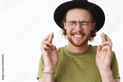 Guy with high hopes making wish, squinting and clenching teeth putting effort in dream come true thought with raised crossed fingers, standing faitful and hopeful over gray background photo