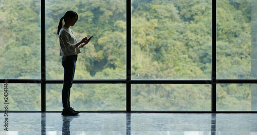 Businesswoman use of mobile phone and walking over the glass window