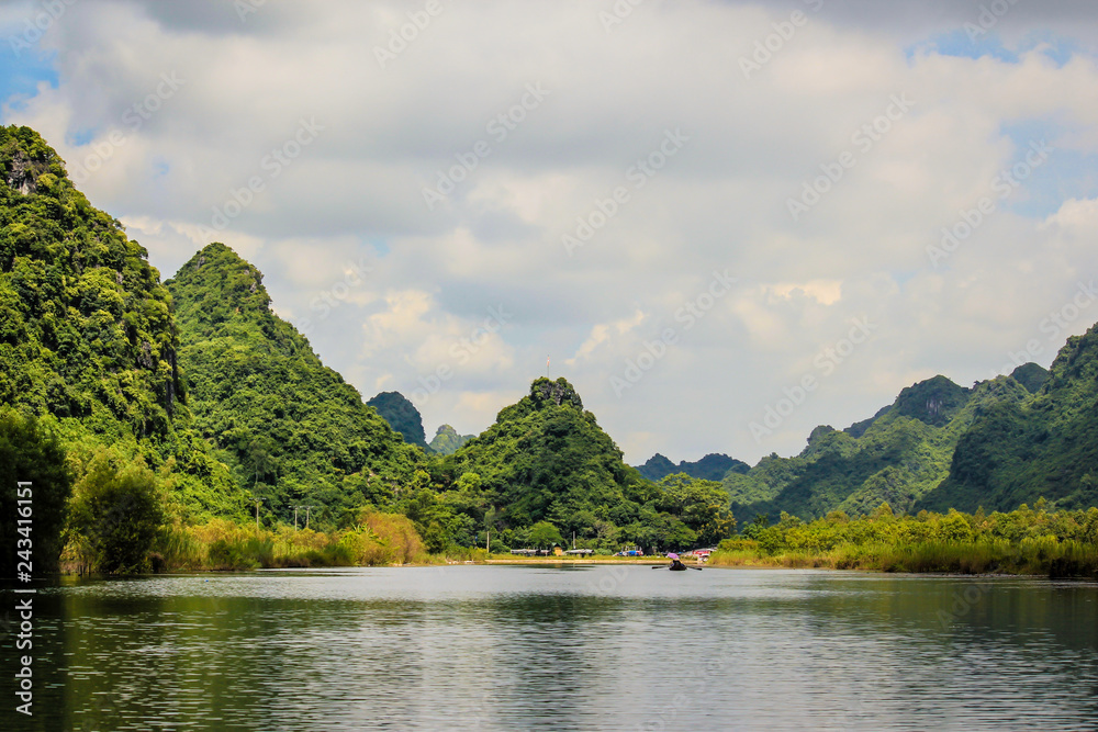 White Clouds and Beautiful Limestone Mountains Covered in Lush Green Vegetation Line the River on the Way to the Perfume Pagoda in Vietnam