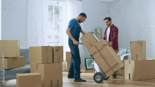 Happy New Homeowner Welcomes Professional Mover with Hand Truck full of Cardboard Boxes, Receives His Goods and Signs on Clipboard.