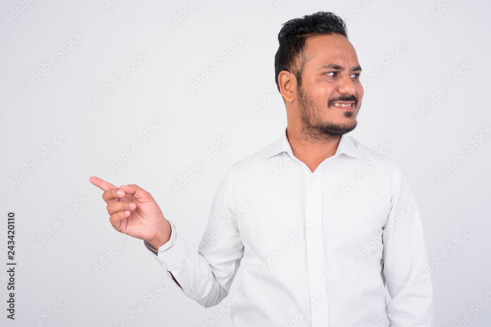 Happy bearded Indian businessman pointing finger and looking to the side Happy bearded Indian businessman pointing finger and looking to the side