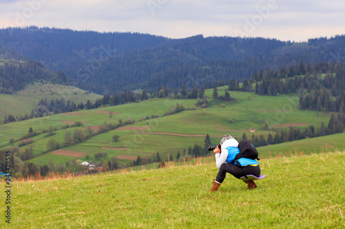 A photographer half crouching shoots the landscape of the Carpathian slopes on a fresh spring morning