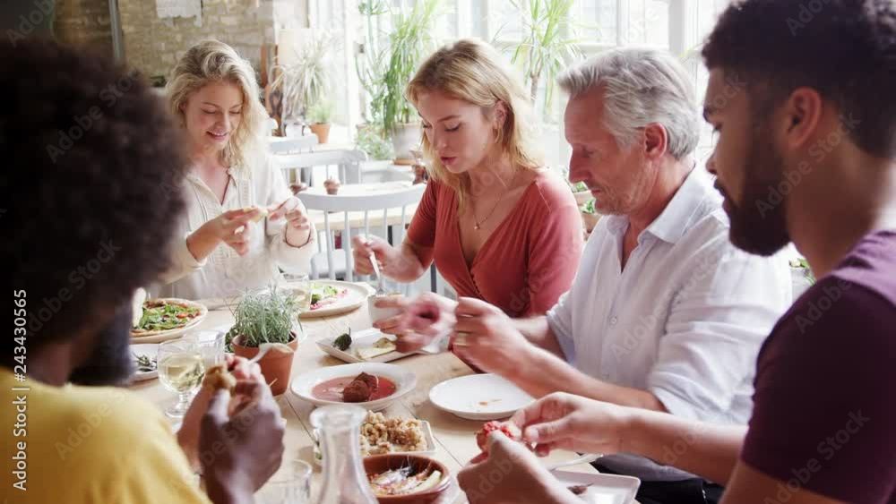 A multi ethnic, mixed age group of adult friends eating tapas together at a table in a restaurant, close up, selective focus