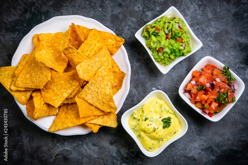 Selection of mexican sauces - salsa, guacamole, cheese sauce and ingredients, dark stone background