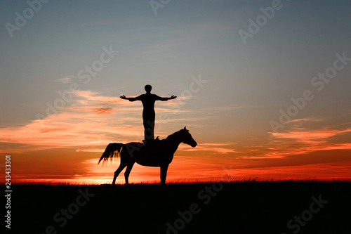 Silhouette of inspired man, standing on horse and with arms raised to sky on bright orange sunset. Unusual amazing horseback, sporty leisure. Fitness, wellness concept on multi-colored sky background.