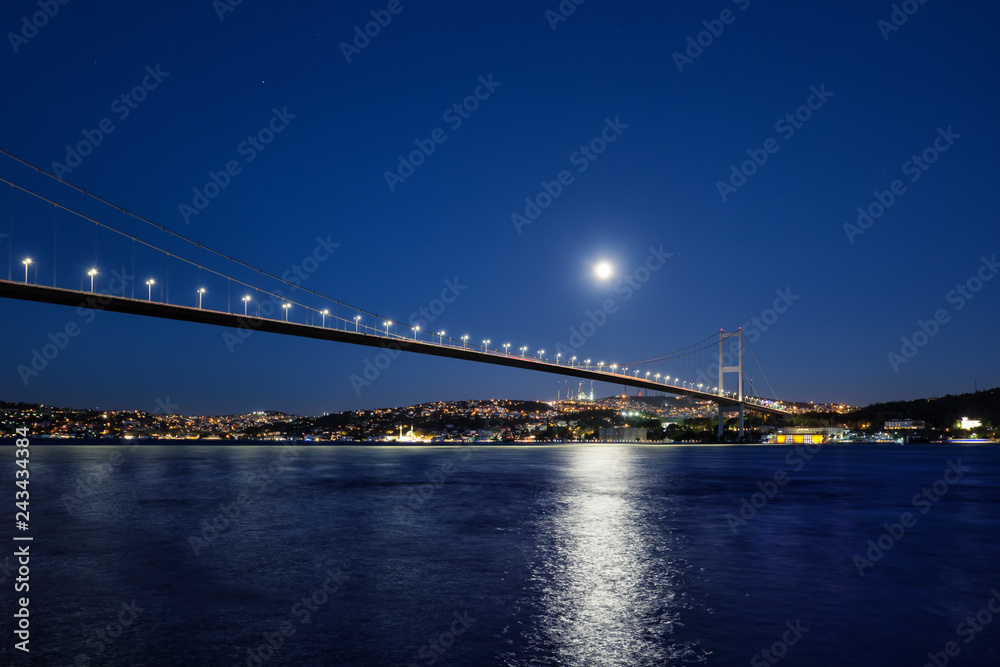 Bosphorus Bridge illuminated by lights and moon at night