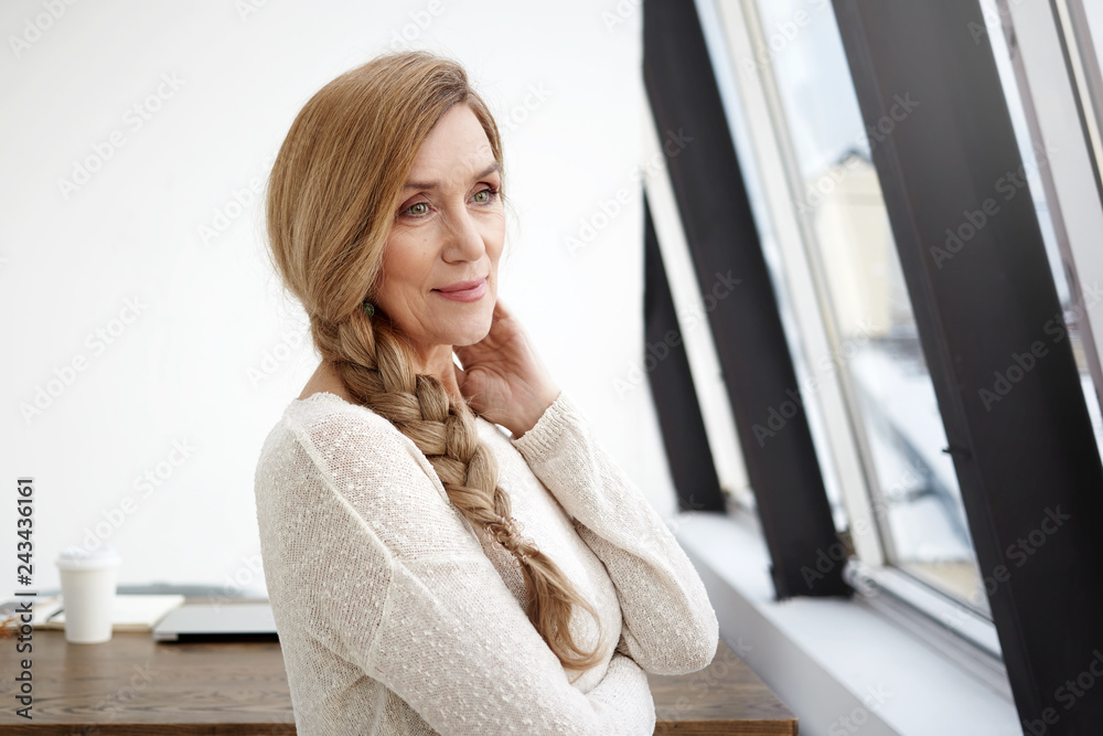 People, style, modern technology, occupation and leisure concept. Picture of elegant gorgeous middle aged mature businesswoman with braid having small break at office, looking through window People, style, modern technology, occupation and leisure concept. Picture of elegant gorgeous middle aged mature businesswoman with braid having small break at office, looking through window