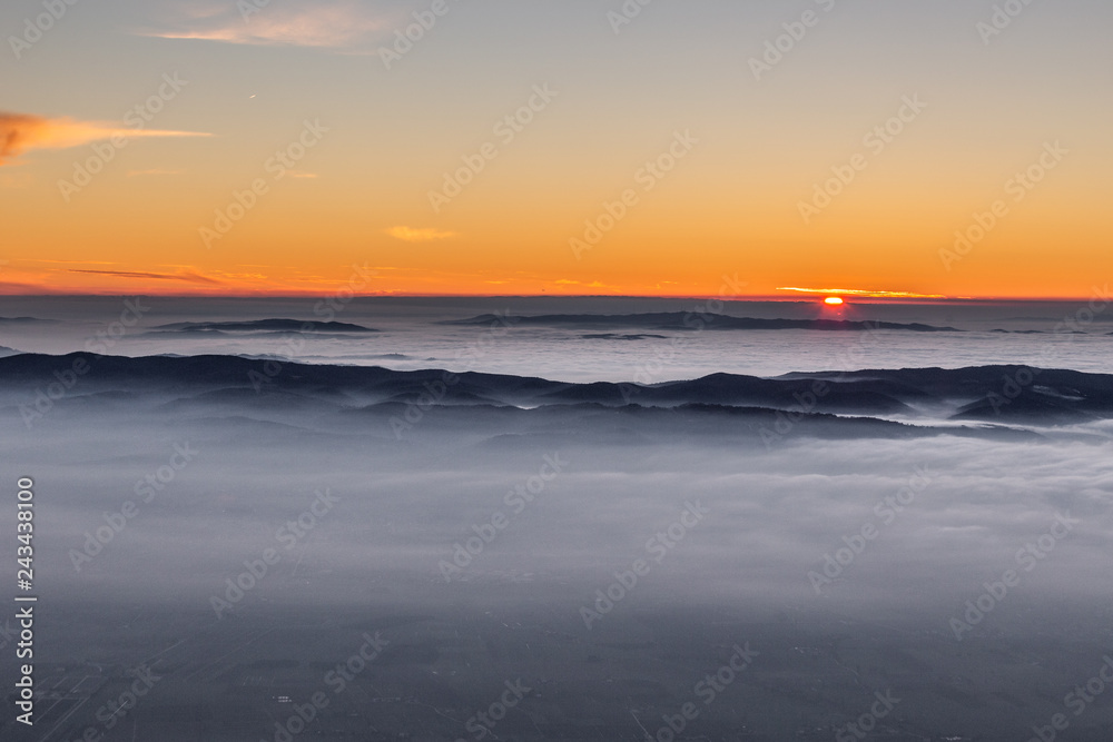 Beautiful sunset over a valley filled by fog with mountains and hills