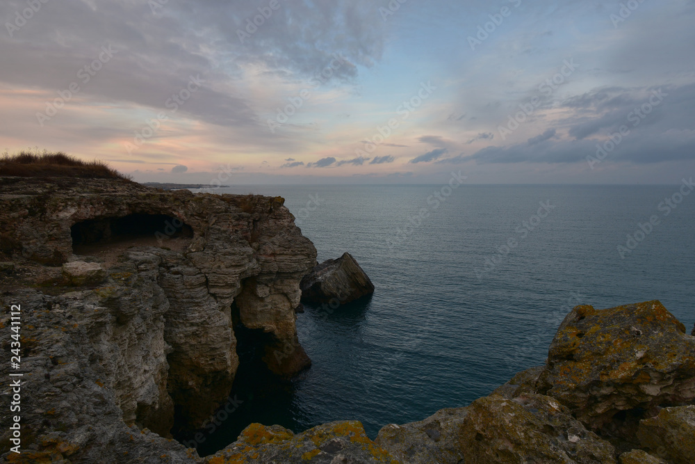 Twilight after sunset. Cliffs with caves rise above the calm see. The Black Sea coast near Tyulenovo, Bulgaria