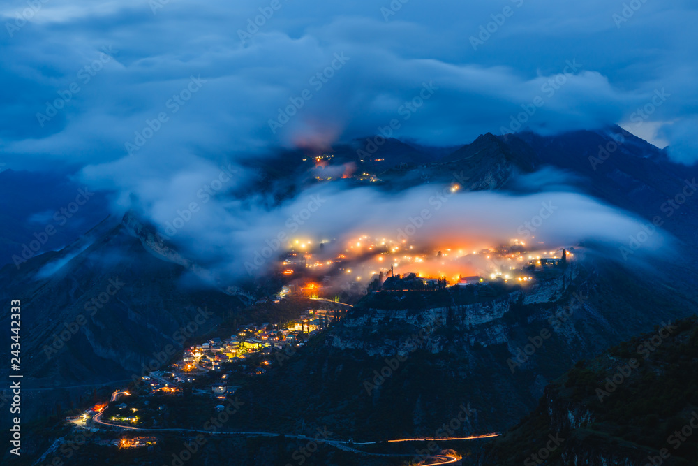 Gunib highland village on a mountain plateau in the clouds with colorful lights at night. Popular tourist place. Beautiful landscape with long exposure. Caucasus Mountains, Dagestan Republic, Russia