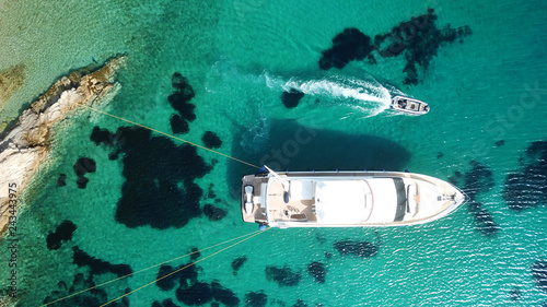 Aerial drone bird's eye top view photo of luxury yacht with wooden deck docked in deep emerald waters of Mykonos island, Cyclades, Greece