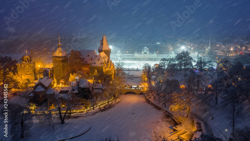 Budapest, Hungary - Aerial view of the beautiful snowy Vajdahunyad Castle at blue hour with Christmas market, ice rink and Heroes' Square at background during snowing