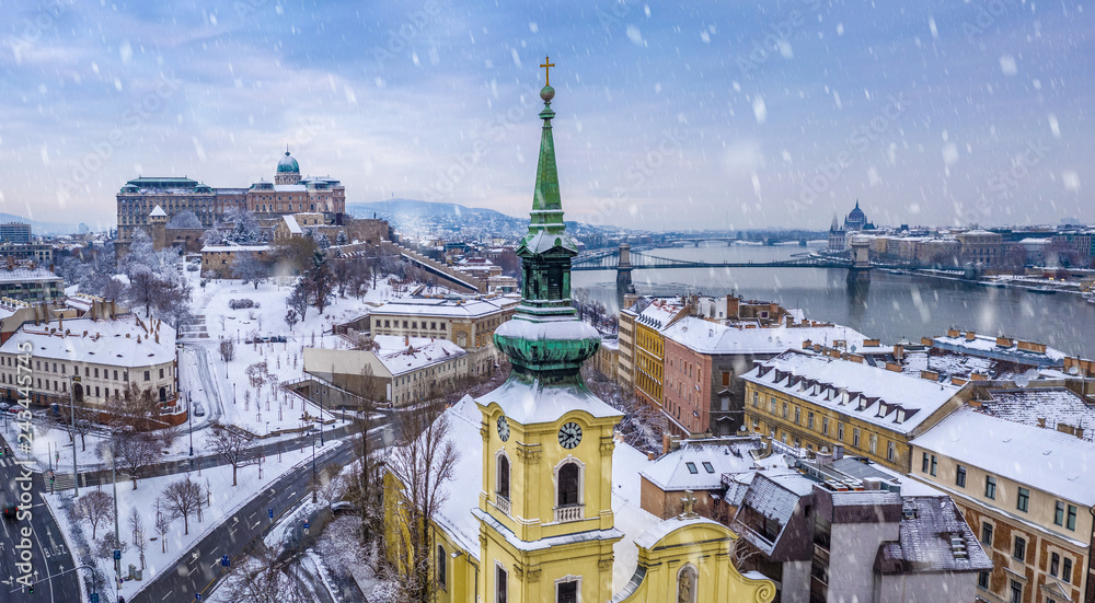 Budapest, Hungary - Catholic church with snowy Buda district, Buda Castle Royal Palace, Varkert Bazaar, Szechenyi Chain Bridge and Parliament at background on a snowy winter morning