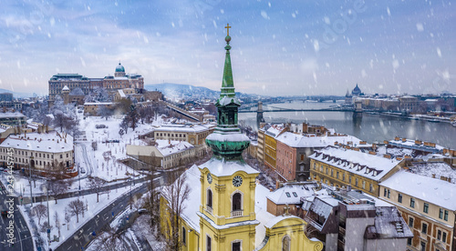 Budapest, Hungary - Catholic church with snowy Buda district, Buda Castle Royal Palace, Varkert Bazaar, Szechenyi Chain Bridge and Parliament at background on a snowy winter morning