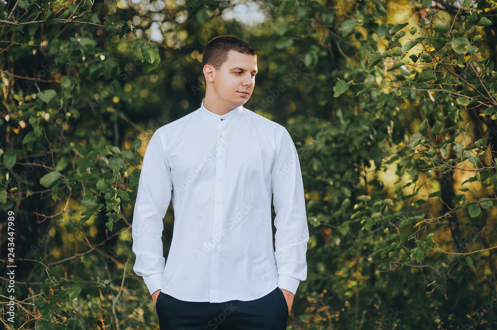 Stylish groom stands in the green garden. Portrait of a handsome man in a white shirt. Wedding photography. Young brunette. Stylish groom stands in the green garden. Portrait of a handsome man in a white shirt. Wedding photography. Young brunette.