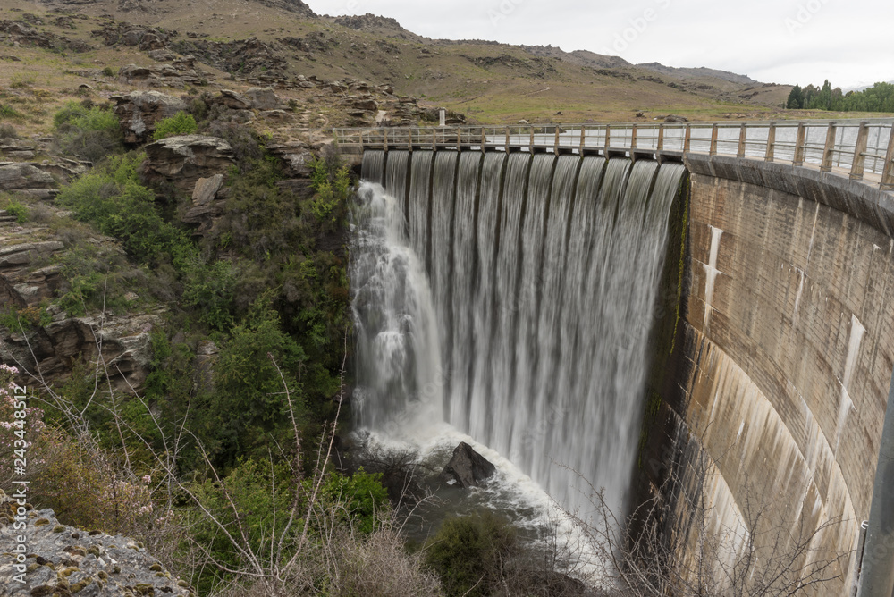 Butcher's Dam, Flat Top Hill Conservation Area, releasing excess water over its spillway. Central Otago, New Zealand.