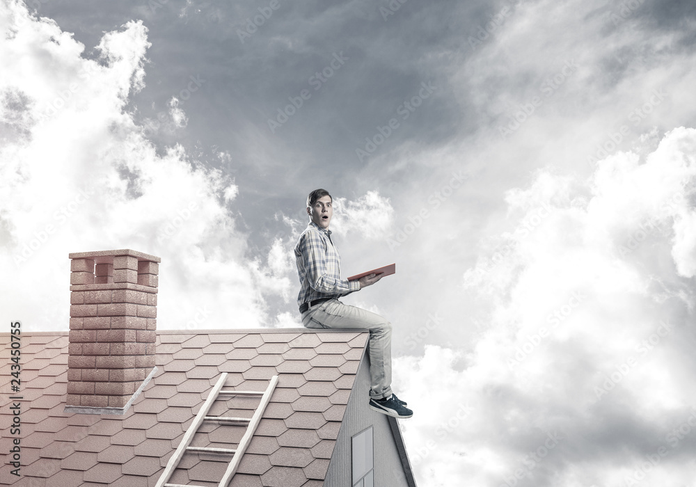 Handsome man on brick roof against cloud scape reading book