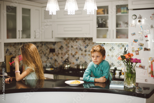 egoism concept little boy brother and small girl sister sitting separately indoors home kitchen