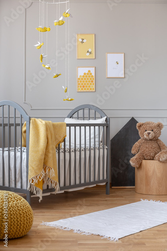 Yellow blanket on grey wooden crib in fashionable baby room with posters on the wall photo