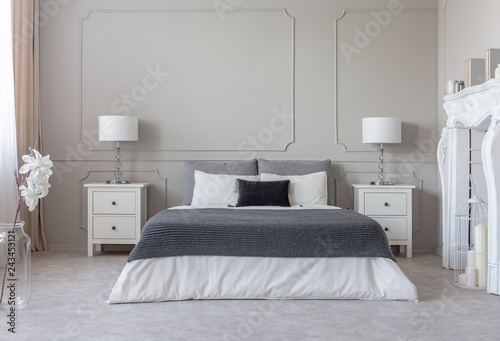 Grey blanket on white bedding on comfortable king size bed  two nightstand with lamps on both sides of it