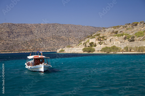 Cruise to the island of Spinalonga. Small boat on the blue lagoon. Spinalonga fortress on the island of Crete, Greece. Architecture on the island.